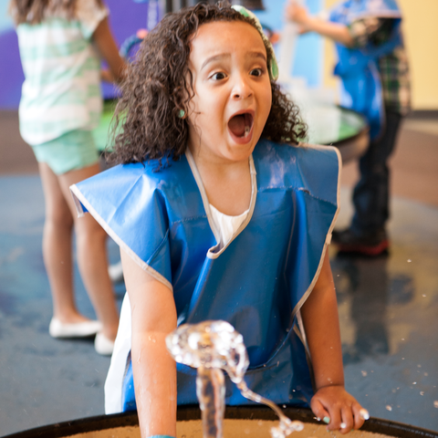 A girl playing at one of the water tables in KidSpace looking surprised